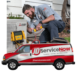 JD Service Now technician inspects a Mitsubishi heat pump outside a home