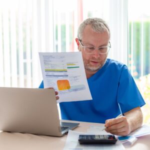 man looking at paperwork with a laptop in front of him