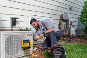 JD Service Now technician inspects AC system outside of a house.
