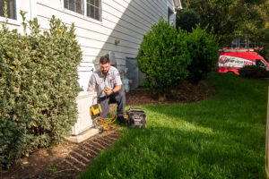 JD Service Now technician inspects AC system outside of a house.