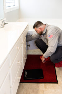 JD Service Now plumber inspects the drain underneath a bathroom sink in a house.