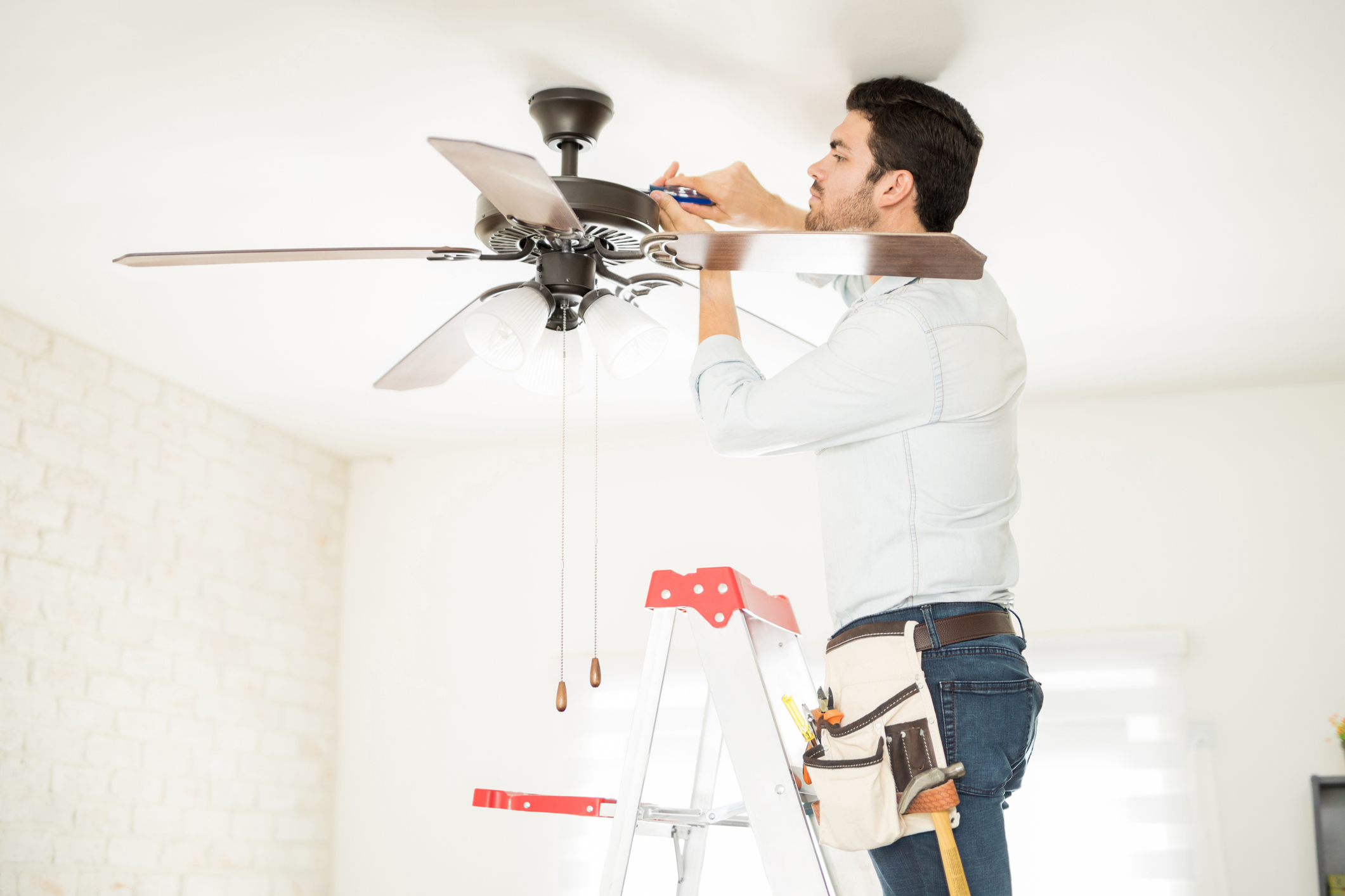 Technician stepping on a ladder and fixing a ceiling fan
