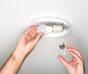 hands replacing a lightbulb in a light fixture in the ceiling