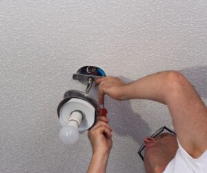 Person installing light fixture into ceiling of a home.