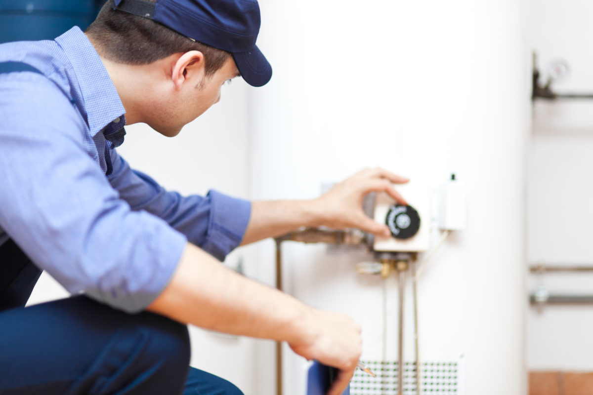 Plumber in blue uniform adjusting the dial on a tank-style water heater