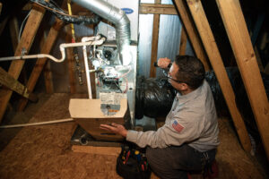 JD Service Now technician inspects the inside of a furnace in an attic.
