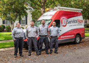 Four JD Service Now technicians stand in a row, in front of truck parked on the side of a tree-lined residential street.