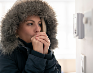 woman in a large jacket in her home, looking cold, stares at a thermometer