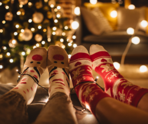 Two pairs of feet in holiday socks with holiday lights in the background.