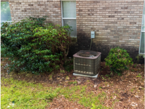 An old HVAC unit sits beside a brick house