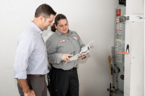 JD Service Now technician points to water heater manual while talking with homeowner.