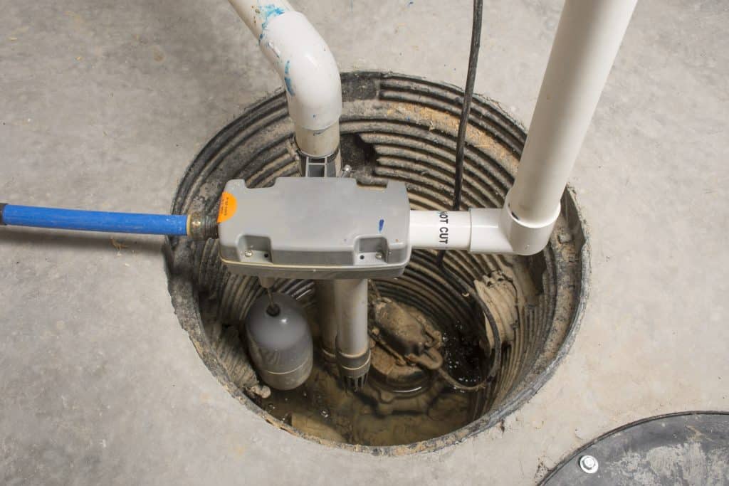 Sump pump installed in a basement pit with PVC plumbing and a float switch.
